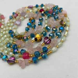 May include: A collection of beaded necklaces featuring a variety of colorful beads. The necklaces include iridescent blue, pink, and gold heart-shaped beads, and light green and pink stone beads. The beads are strung on gold-colored wire.