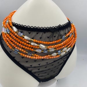 May include: A black lace lingerie set with a beaded waist chain. The waist chain features orange, blue, and white beads. The lingerie is displayed on a white mannequin.