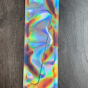May include: A silver-colored metal tool with a curved hook shape, packaged in a holographic iridescent plastic bag.