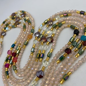 May include: Several beaded necklaces in a variety of colours. The necklaces feature small, iridescent beads in a pale pink hue, with colourful accent beads in green, purple, and gold. The necklaces are layered, displaying the intricate beadwork.