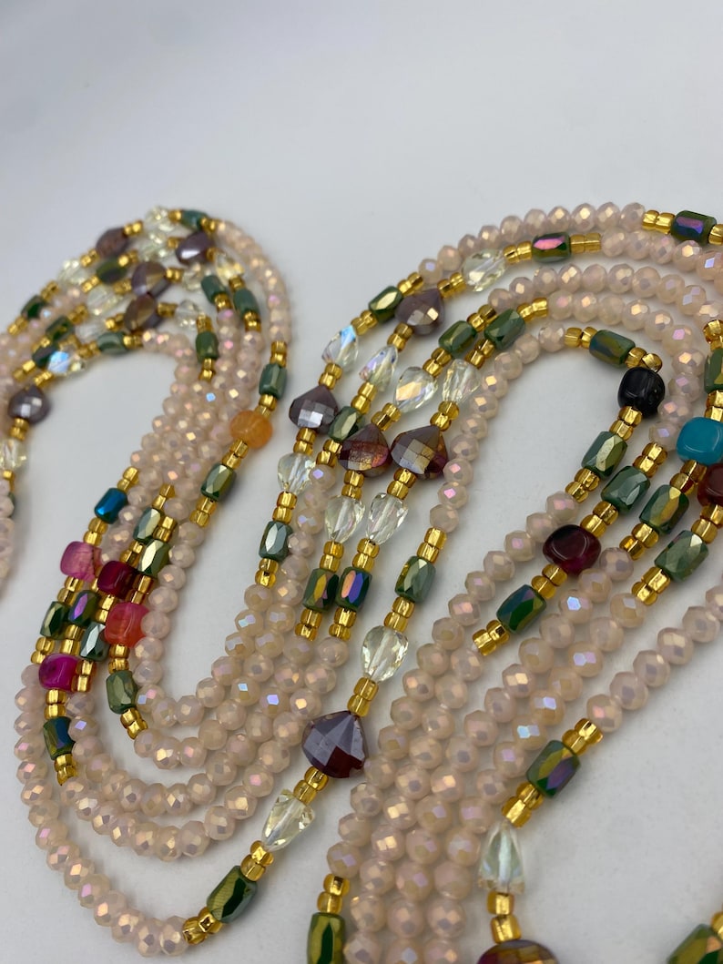 May include: Several beaded necklaces in a variety of colours. The necklaces feature small, iridescent beads in a pale pink hue, with colourful accent beads in green, purple, and gold. The necklaces are layered, displaying the intricate beadwork.