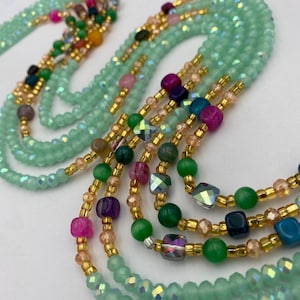 May include: Mint green beaded waist beads with gold accents and colourful beads. The strands feature a mix of round and faceted beads in shades of pink, green, purple, and blue. The beads are strung together with gold-coloured string.