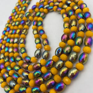 May include: Close-up of multiple beaded necklaces. The necklaces combine yellow, iridescent, and silver beads. The yellow beads are faceted, while the iridescent beads have a metallic sheen with colours like purple, blue, and green. The beads are strung together.