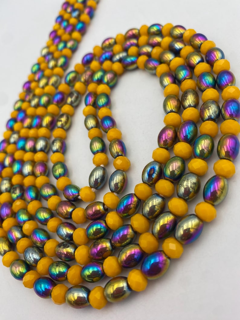 May include: Close-up of multiple beaded necklaces. The necklaces combine yellow, iridescent, and silver beads. The yellow beads are faceted, while the iridescent beads have a metallic sheen with colours like purple, blue, and green. The beads are strung together.
