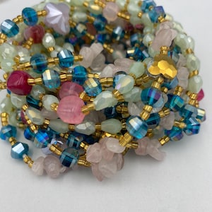May include: A collection of colorful beaded jewelry. The beads are in shades of pink, blue, green, and gold. The beads are strung together with gold-colored wire. The jewelry is likely a necklace or bracelet.