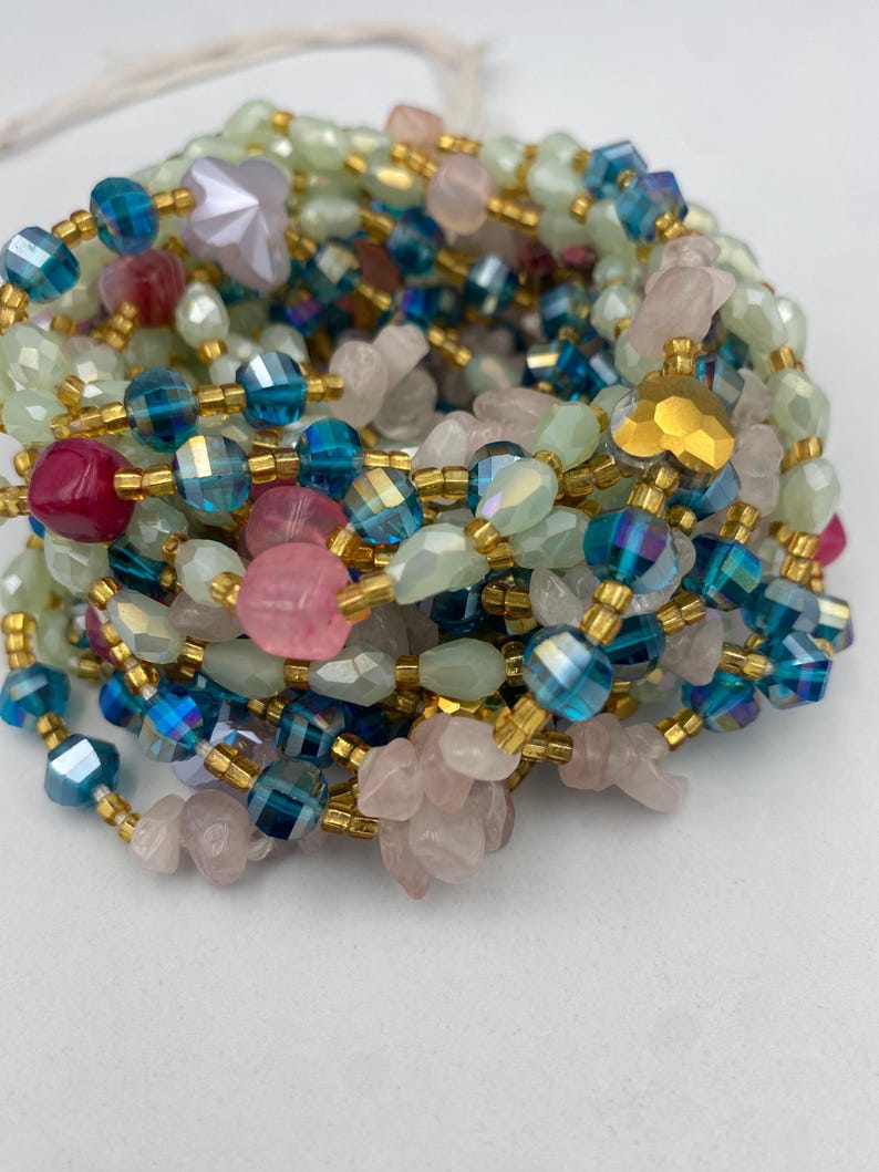 May include: A collection of colorful beaded jewelry. The beads are in shades of pink, blue, green, and gold. The beads are strung together with gold-colored wire. The jewelry is likely a necklace or bracelet.