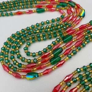 May include: A selection of beaded necklaces in green, red, and gold. The necklaces feature small, round beads and larger, faceted beads. The beads are strung together with gold-coloured string, creating a layered effect. The design is colourful and eye-catching.