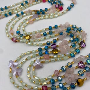 May include: Several layered necklaces with a variety of beads in shades of pink, blue, and green. The necklaces feature gold-colored accents and include butterfly and heart-shaped beads. The beads are strung together with gold-colored wire.