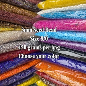 May include: A collection of 3mm seed beads in size 8/0, packaged in clear plastic bags weighing 450 grams each. The assortment features a wide variety of vibrant colors including red, yellow, green, blue, purple, orange, silver, and gold tones.