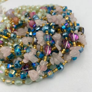 May include: A collection of beaded necklaces in various colors. The necklaces feature iridescent blue, pink, and green beads, along with gold-colored spacers and rose quartz chips. The beads are strung together, creating a layered effect.