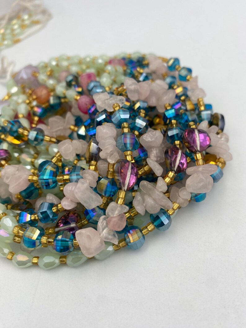 May include: A collection of beaded necklaces in various colors. The necklaces feature iridescent blue, pink, and green beads, along with gold-colored spacers and rose quartz chips. The beads are strung together, creating a layered effect.