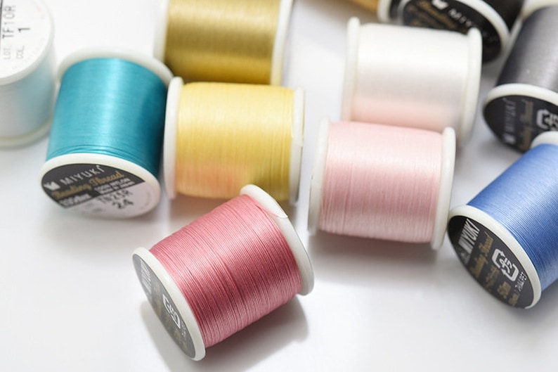 May include: Assortment of spools of embroidery thread in various colors, including teal, yellow, pink, and blue. The spools are labeled "Miyuki Beading Thread".