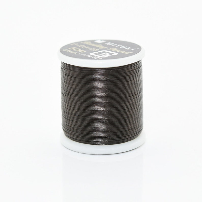 May include: A spool of black waxed thread for sewing or crafts. The spool is labeled "Miyuki" and "100% Polyester - Thread".