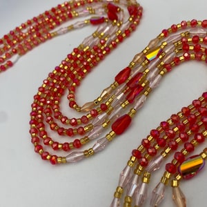 May include: Close-up of multiple strands of red and gold beaded jewellery. The beads are small and faceted, with a mix of red, gold, and iridescent accents. The strands are arranged in a layered pattern, creating a textured and eye-catching design.