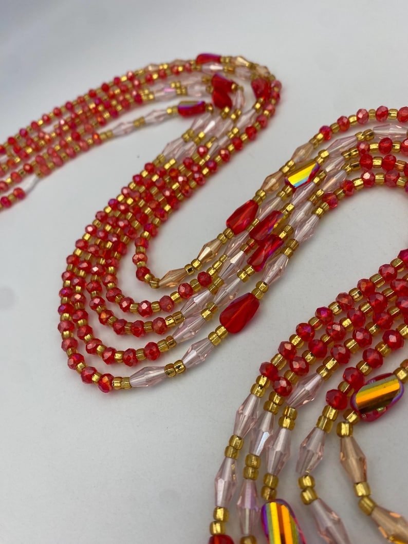 May include: Close-up of multiple strands of red and gold beaded jewellery. The beads are small and faceted, with a mix of red, gold, and iridescent accents. The strands are arranged in a layered pattern, creating a textured and eye-catching design.