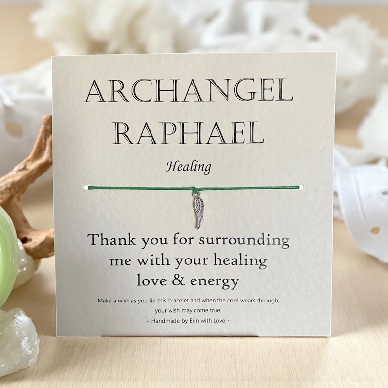 May include: A square card with the words "ARCHANGEL RAPHAEL Healing" printed in black. A green string bracelet with a silver wing charm is attached. The card reads "Thank you for surrounding me with your healing love & energy."