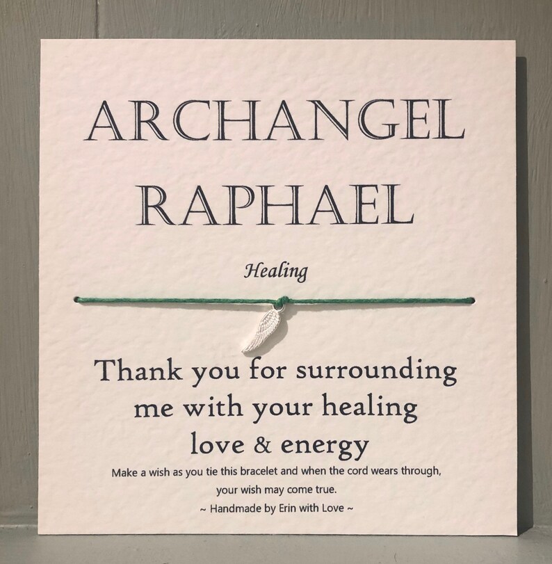 May include: A square card with the words "ARCHANGEL RAPHAEL" and "Healing" printed in black. A green string is attached with a small silver feather charm. The text "Thank you for surrounding me with your healing love & energy" is also printed.