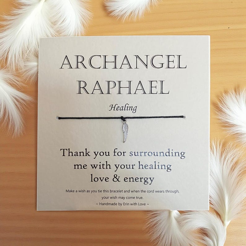 May include: A greeting card with the words "ARCHANGEL RAPHAEL Healing" and a black string bracelet with a silver wing charm. The card also includes the text "Thank you for surrounding me with your healing love & energy."