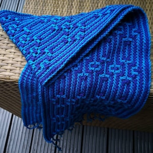 May include: A blue and purple crocheted blanket with a geometric pattern. The blanket is folded in half and has a fringe on the bottom edge.