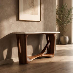 May include: A modern console table with a white marble top and a dark wood base. The base features a unique, curved design with open spaces. The table is placed against a neutral-colored wall, with a framed artwork above it.