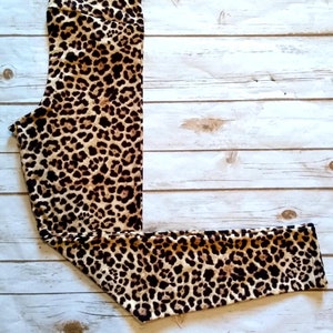 May include: High-waisted leggings featuring a leopard print design. The leggings are predominantly tan with dark brown spots. They are displayed on a light-coloured wooden surface.