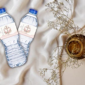 Puede incluir: Dos botellas de agua de plástico transparente con etiquetas rosas y blancas que muestran una cruz y un diseño floral. Las etiquetas tienen el texto "Primera Comunión" impreso.