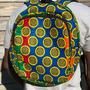 Puede incluir: Una mochila azul con un patrón de girasol amarillo. La mochila tiene rayas rojas, verdes y naranjas en los lados.