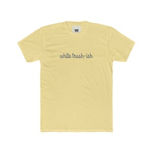 May include: A pale yellow t-shirt with the text "white trash-ish" printed in gray on the front.