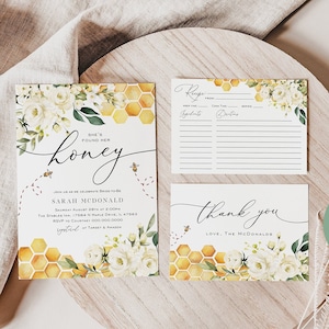 May include: A set of printable bridal shower invitations with a honeybee theme. The invitation features a watercolour illustration of white flowers and a honeycomb pattern. The text on the invitation reads "She's found her honey" and includes the bride's name, date, time, and location. The set also includes a recipe card and a thank you card.