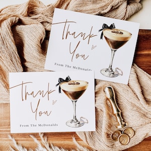 May include: Two white cards with the words "Thank You" in elegant brown script, featuring a cocktail illustration with coffee beans and a black bow. The cards are on a wooden tray with a gold wax seal.