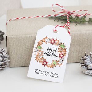 May include: White gift tag with a red and white twine bow. The tag has a hand-drawn illustration of a wreath made of gingerbread cookies with the text "baked with love". The text "With love from The McDonalds" is printed below the illustration.