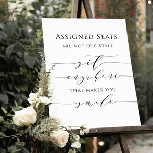 May include: White sign with black text on an easel. The sign reads "Assigned Seats Are Not Our Style Sit Anywhere That Makes You Smile".