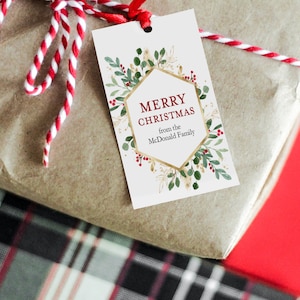 May include: A white gift tag with a gold hexagonal frame and green and red floral accents. The text on the tag reads "Merry Christmas from the McDonald Family".