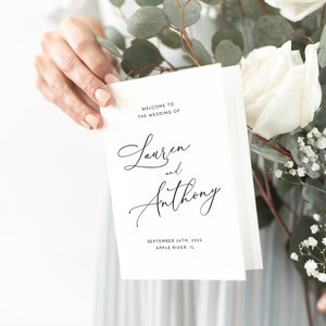 May include: A white wedding invitation card with black calligraphy text. The text reads "Welcome to the wedding of Lauren and Anthony, September 24th, 2023, Apple River, IL."
