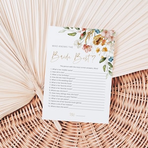 May include: A white card with a floral design and the text "WHO KNOWS THE Bride Best?"  The card has a list of questions about the bride, such as "What is her middle name?" and "What is her favorite drink?"