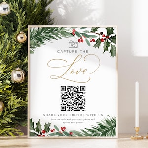 Op de afbeelding: Een wit bord met een groene en rode rand van hulst. Het bord zegt "Capture the Love" in gouden schrift met een camera-icoon en een QR-code. De tekst onder de QR-code zegt "Deel je foto's met ons. Scan de code met je smartphone en upload je foto's."