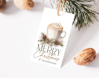 May include: A white gift tag with a watercolor illustration of a cup of coffee with whipped cream and pine branches. The text "Merry Christmas" is written in black with a gold outline. The text "The McDonalds" is written in black below the greeting.