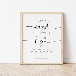 May include: A printable sign with black text on a white background in a wooden frame. The text reads "Take a wand and wave it high as the happy couple passes by!" with a heart symbol and the names "Courtney & Steven".