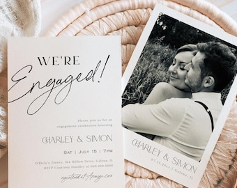 May include: Engagement announcement cards with the text "WE'RE Engaged!" in elegant script. The cards include details for the celebration, and a black and white photo of the couple. The cards are on a woven mat.