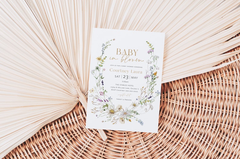 May include: A white baby shower invitation with a floral wreath design. The text reads "Baby in Bloom" and includes the name "Courtney Laura" and the date "Sat 23 | May".