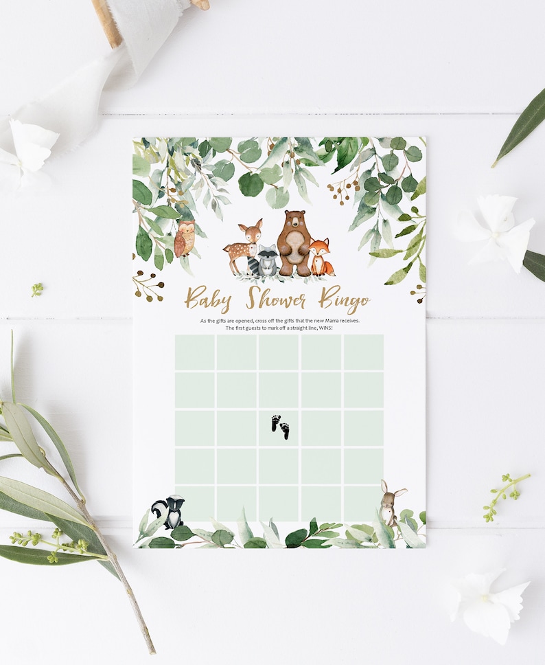 May include: A green and gold baby shower bingo card with a woodland animal theme. The card has a grid of squares with images of a bear, owl, deer, raccoon, fox, skunk, bunny, and footprints. The text "Baby Shower Bingo" is at the top of the card.