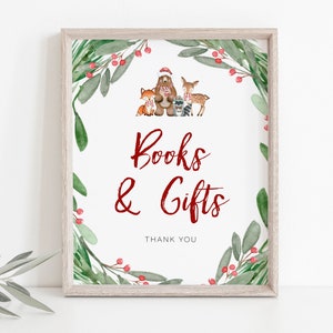 Puede incluir: Un cartel blanco con un borde de corona de acuarela verde y roja. La corona presenta un oso, un zorro, un mapache y un ciervo con gorros y bufandas de invierno. El cartel dice "Libros & Regalos" en rojo con "Gracias" debajo.