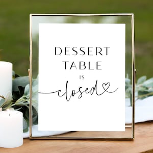 May include: A white sign with black text in a gold frame that reads "Dessert Table is closed" with a heart symbol.
