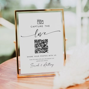 May include: A white sign with a gold frame, featuring a black and white QR code, the text "Capture the love", and the names "Sarah & Anthony".