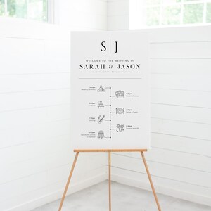 May include: White wedding welcome sign with black text and icons. The sign reads "Welcome to the wedding of Sarah & Jason" and lists the wedding day schedule with times and icons for each event.