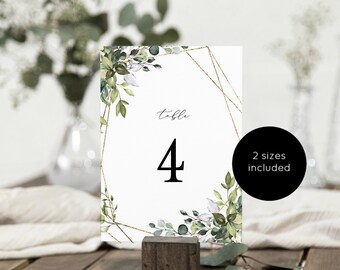 May include: A white table number card with a gold geometric frame and green watercolor foliage. The card says "table 4" in black text.