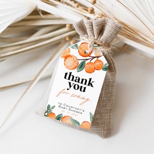 May include: A white thank you tag with orange citrus fruit illustrations and the text "thank you for coming to Courtney's Baby Shower 08.11.20xx". The tag is tied to a small burlap bag.