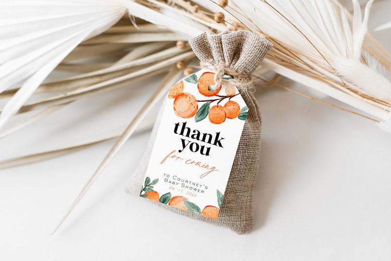 May include: A white thank you tag with orange citrus fruit illustrations and the text "thank you for coming to Courtney's Baby Shower 08.11.20xx". The tag is tied to a small burlap bag.