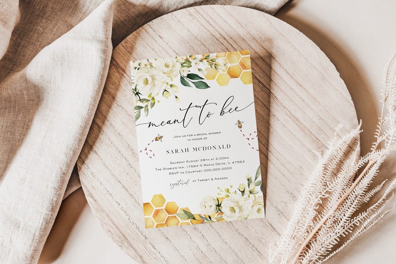 May include: A white card with a watercolor design of white flowers and a honeycomb pattern. The text on the card reads "meant to bee" and includes details for a bridal shower for Sarah McDonald.