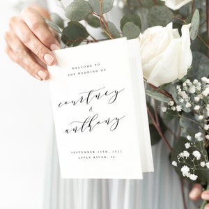 May include: A white wedding invitation card with black calligraphy text that reads "Welcome to the wedding of Courtney & Anthony" and the date "September 24th, 2022" and location "Apple River, IL".